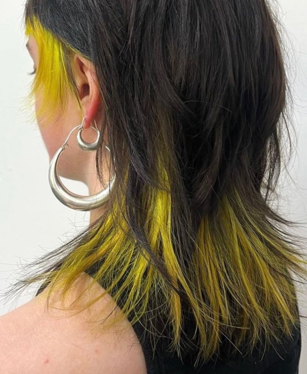 Side view of a person with black hair and yellow dyed tips, wearing large silver hoop earrings on the ear and neck area visible.