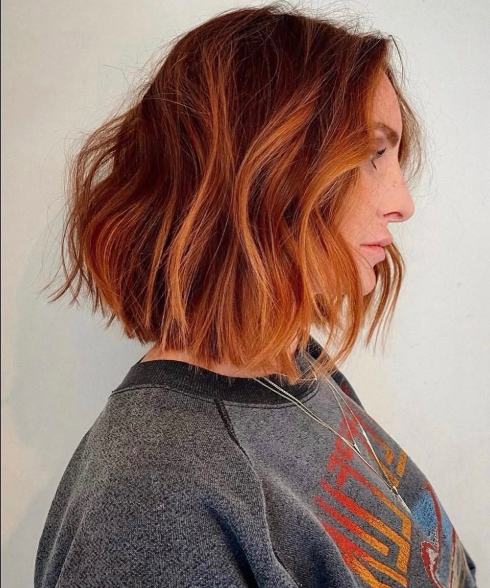 Side profile of a woman with shoulder-length, wavy copper hair wearing a gray sweatshirt.